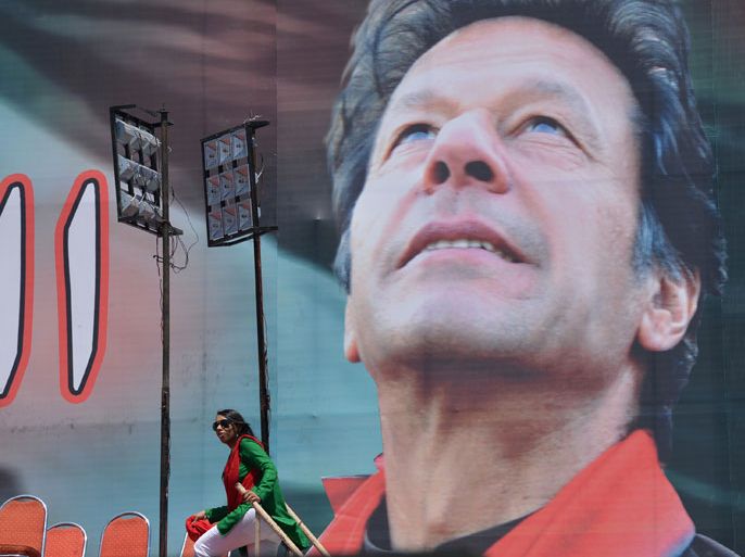 A supporter of Pakistani politician and former cricketer Imran Khan walks onto a stage next to an electoral poster of Khan at the venue of an election campaign meeting by Khan's party Pakistan Tehreek-e-Insaf (PTI) in Islamabad on May 9, 2013. Khan will address the final rally for his centre-right Pakistan Tehreek-e-Insaf party in the capital Islamabad by live video link from his Lahore hospital bed. Saturday's vote will be a democratic milestone in a country ruled for half its history by the military but the Pakistani Taliban have condemned it as un-Islamic. AFP PHOTO / AAMIR QURESHI