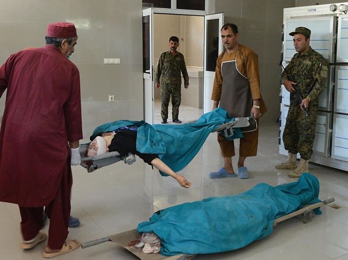 Afghan medical workers carry the bodies of two foreign women who were gunned down by men on a motorcycle, at the morgue of Herat hospital on July 24, 2014. Two foreign female aid workers were shot dead by unknown gunmen while travelling in a taxi in the western Afghan city of Herat, officials said. AFP PHOTO/Aref Karimi
