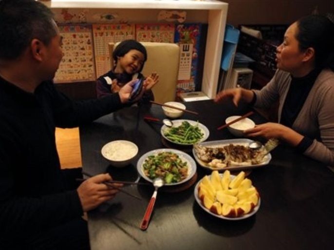 In this photo taken Wednesday, March 16, 2011, five years old Zhong Chuhan, center reacts as her mother, Li Mingxia, right, and her father Zhong Sheng, left, coaxs her from her game to eat dinner at their home in Beijing, China. The starkly contrasting fortunes of two Chinese families, one affluent and one low income, offer a glimpse into how soaring food prices are playing out in the developing world. Rising affluence has taxed the ability of farmers to meet growing demand while the rural labor pool dwindles. The result: Rising food prices hit those on fixed or stagnant incomes hardest.