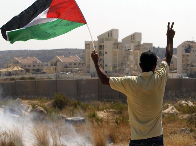 A Palestinian demonstrator waves his national flag as he flashes the sign for victory during clashes with Israeli security personnel in the village of Bilin, near the West Bank city of Ramallah after a march in support of the resistance in the Gaza Strip on August 29, 2014. Seven weeks of war between Hamas militants and Israel in Gaza killed more than 2,100 people and and left the territory's infrastructure in tatters and tens of thousands of Palestinians displaced. AFP PHOTO / ABBAS MOMANI