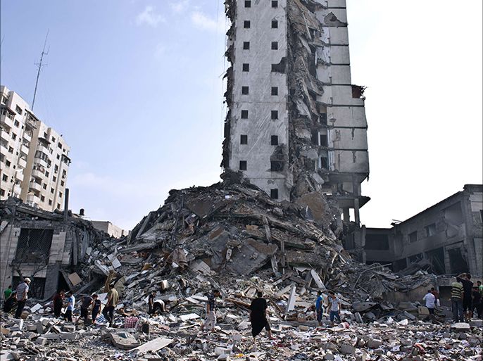Palestinians walk at the base of what used to be a high rise apartment building in Gaza City that was targeted by Israeli air strikes overnight on August 26, 2014