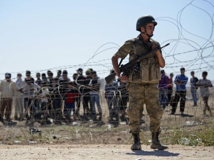 A Turkish soldier stands guard as Syrian Kurds wait behind the border fence near the southeastern town of Suruc in Sanliurfa province, September 21, 2014. Kurdish militants in Turkey have issued a new call to arms to defend a border town in northern Syria from advancing Islamic State fighters, and the Turkish authorities and United Nations prepared on Sunday for a surge in refugees. About 70,000 Syrian Kurds have fled into Turkey since Friday as Islamic State fighters seized dozens of villages close to the border and advanced on the frontier town of Ayn al-Arab, known as Kobani in Kurdish. REUTERS/Stringer (TURKEY - Tags: POLITICS MILITARY CIVIL UNREST CONFLICT SOCIETY IMMIGRATION)
