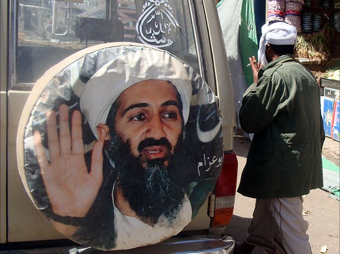 epa03071314 An al-Qaeda-linked fighter walks past a poster of the late head of al-Qaeda Osama bin Laden, while patrolling at a street in the southeast town of Rada, Yemen, 21 January 2012. According to media sources, Yemeni tribal