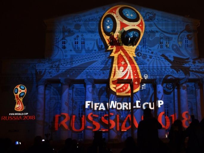 People watch as the facade of the historical Bolshoi Theatre is illuminated with the official emblem of the 2018 FIFA World Cup to be held in Russia in central Moscow on late October 28, 2014. World football boss Sepp Blatter on Tuesday opposed any boycott of the 2018 World Cup in Russia and backed the huge preparations undertaken by President Vladimir Putin's government for the mega event. AFP PHOTO/KIRILL KUDRYAVTSEV