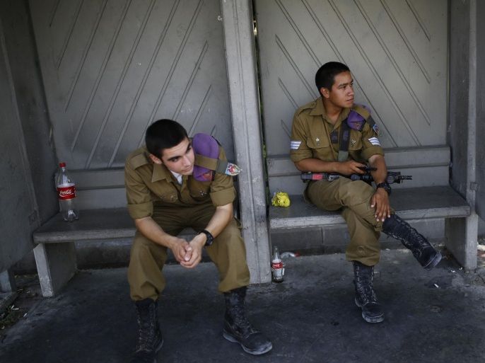 Israeli soldiers wait at a bus stop at Kibbutz Yad Mordechai near the border with northern Gaza August 28, 2014. An open-ended ceasefire in the Gaza war held on Wednesday as Prime Minister Benjamin Netanyahu faced strong criticism in Israel over a costly conflict with Palestinian militants in which no clear victor has emerged. REUTERS/Amir Cohen (ISRAEL - Tags: POLITICS CONFLICT CIVIL UNREST MILITARY)