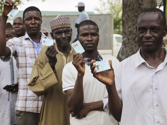 Men show their new electoral cards while queuing at a accreditation center in Abuja on March 28, 2015. After weeks of delays over an Islamic insurgency, Nigerians head to the polls on March 28 to elect a president for Africa's biggest economy. AFP PHOTO / STRINGER