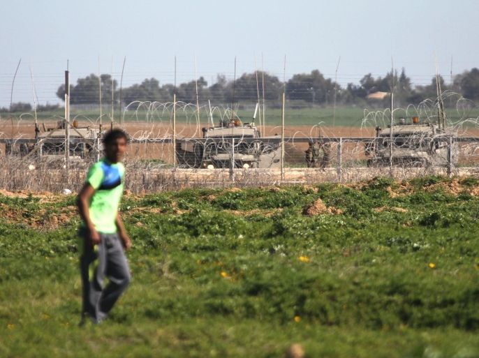 A Palestinian walks past a fence with Israeli solders on the other side near a protest against Israel and their blockade of Gaza in Khan Yunis in the southern Gaza Strip on February 1, 2015. Israel imposed a blockade on Gaza in 2006, and has built an electric fence and buffer zone that are meant to make it virtually impossible for anyone to infiltrate the Jewish state. AFP PHOTO/ SAID KHATIB