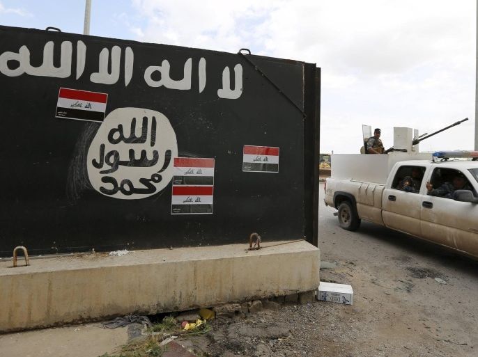 Iraqi security forces ride a vehicle past a wall painted with the black flag commonly used by Islamic State militants, near former Iraqi president Saddam Hussein's palace in Tikrit April 1, 2015. The Iraqi government claimed victory over Islamic State insurgents in Tikrit on Wednesday after a month-long battle for the city supported by Shi'ite militiamen and U.S.-led air strikes, saying that only small pockets of resistance remained. REUTERS/Thaier Al-Sudani