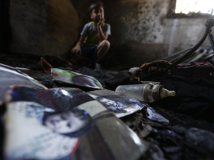Burnt photographs of 18-month-old Ali Dawabsha are seen in Ali's fire damaged room in the West Bank village of Douma near Nablus City, 31 July 2015. The Palestinian infant was killed and several people injured when their home was set alight in the northern West Bank early 31 July 2015, an official said. A group of masked people believed to be Israeli settlers threw flammable bombs into two houses on the outskirts of the village of Doma, south of Nablus, said Ghassan Daghlas, a Palestinian Authority official.