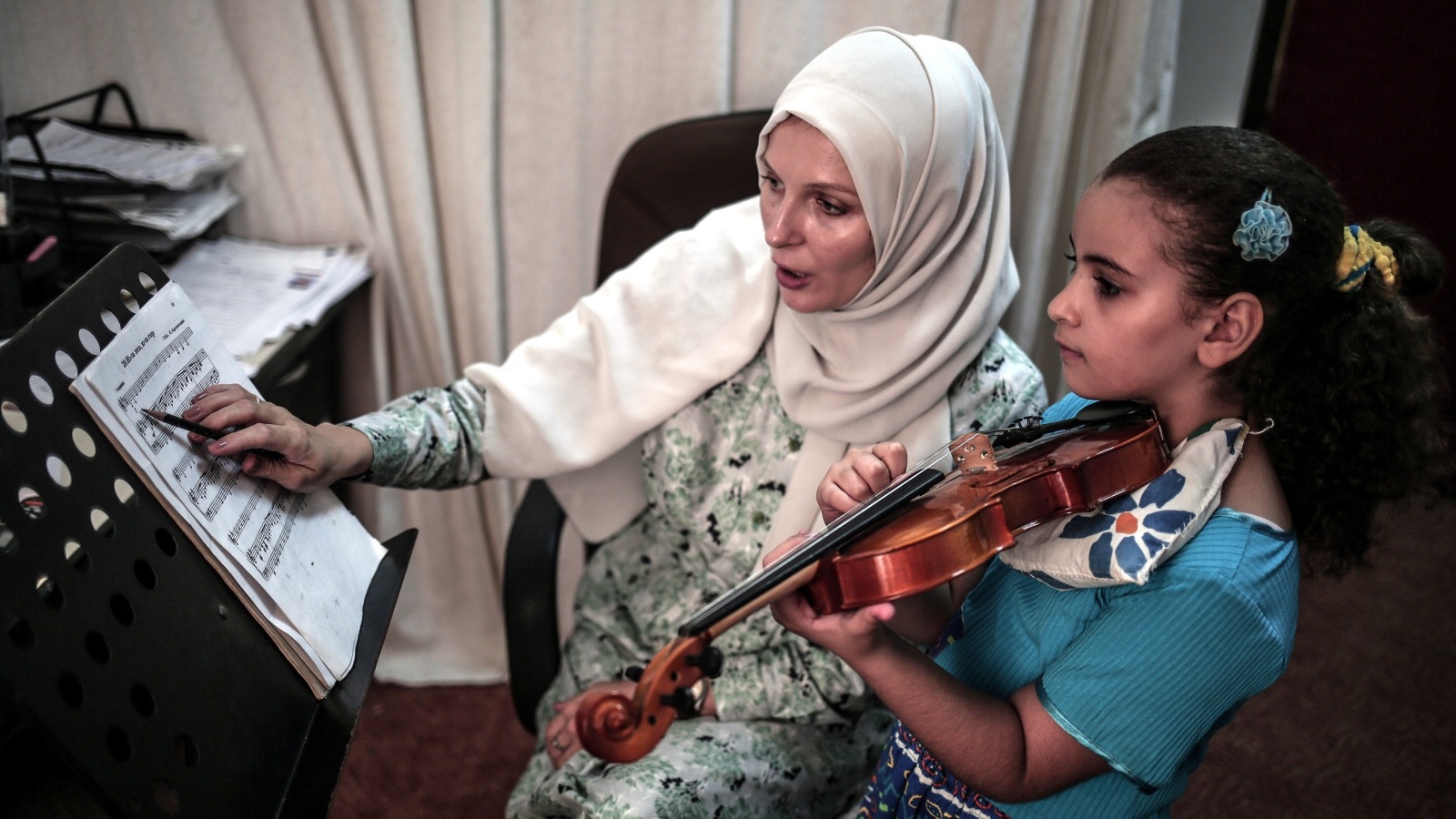 طفلة فلسطينية تتدرب مع معلّمتها على تأدية مقطوعة موسيقية بآلة الكمان (الأناضول)