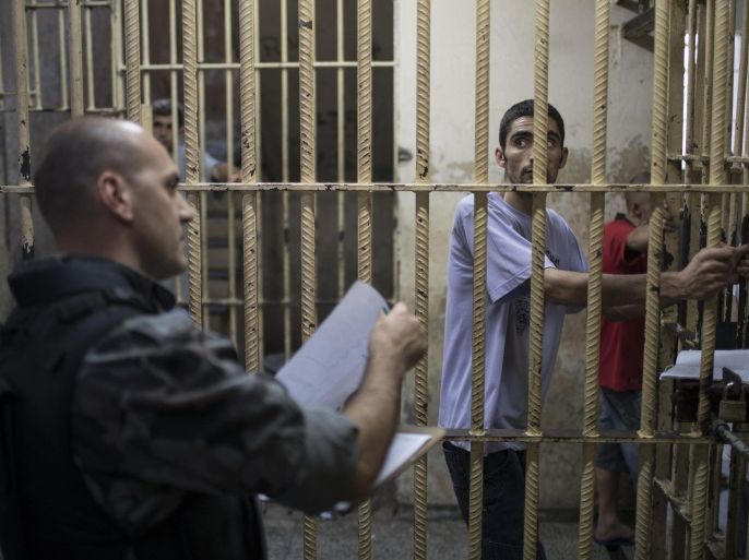 In this Dec. 1, 2015 photo, an inmate watches a police officer take a prisoner count inside the Central Prison in Porto Alegre, Brazil. Prisoners are housed in different cells according to which gangs they belong to in an effort to tamp down violence. (AP Photo/Felipe Dana)