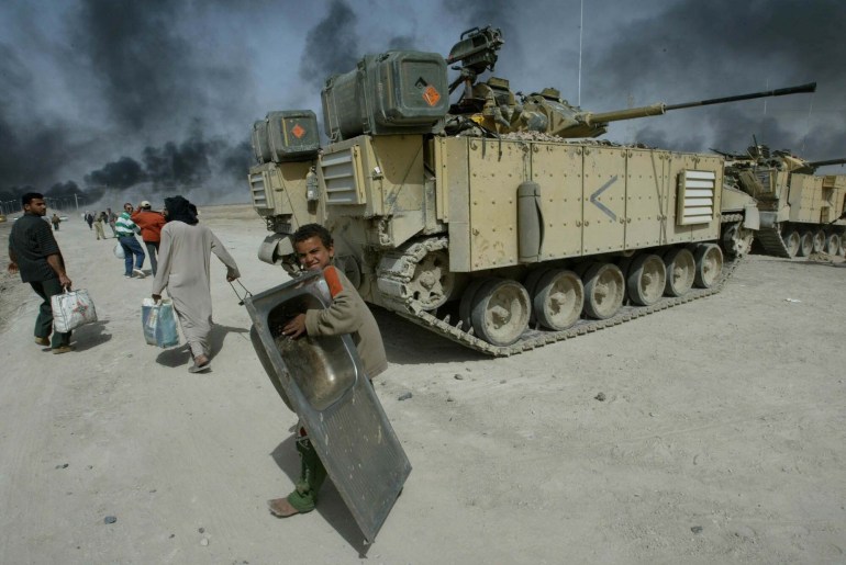 An Iraqi boy carries a sink as passes a British tank outside Basra in southern Iraq as smohe ke looming over the city can be seen in the distance Saturday, March 29, 2003. (AP Photo/Anja Niedringhaus)