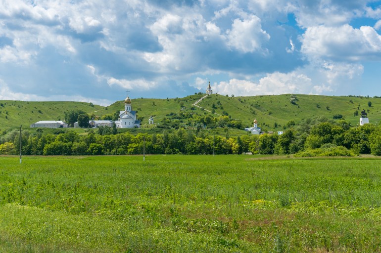 Nature landscape with green grass meadow and churches of Christian monastery with golden cupolas, domes. Holkovsky Monastery, Russia; Shutterstock ID 1557336005; purchase_order: ajanet; job: ; client: ; other: