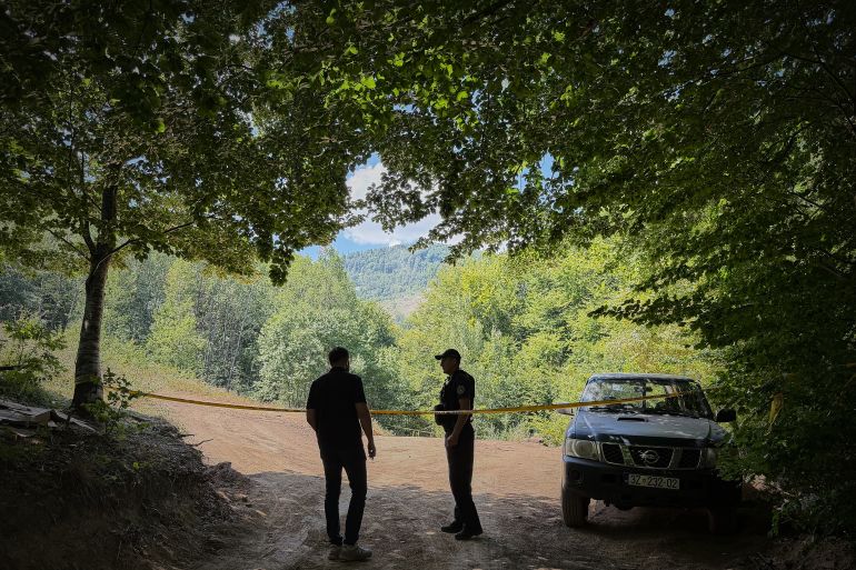 Erblin Ademi, left, whose father, Adem Ademi, a prominent surgeon, disappeared along with 22 other intellectuals during the Kosovo war in April 1999, speaks to a police officer near the excavation site of a mass grave in Small Kalluder, Kosovo, Wednesday, Aug. 5, 2026. (AP Photo/Zana Cimili)