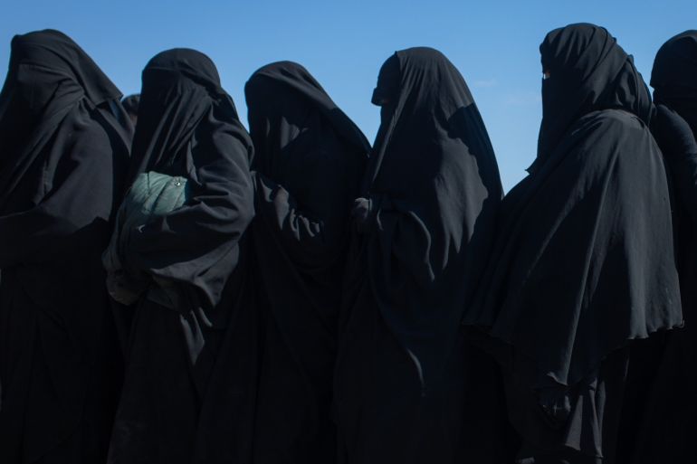 DEIREZZOR, SYRIA - FEBRUARY 16: A woman clutches her handbag as she stands in line with other women who fled fighting in Bagouz after being screened by members of the Syrian Democratic Forces (SDF) at a makeshift screening point in the desert on February 12, 2019 in Bagouz, Syria. Civilian numbers fleeing fighting have increased in recent days after the beginning of a final operation by the US-led coalition and the Syrian Democratic Forces (SDF) to oust ISIS from Bagouz