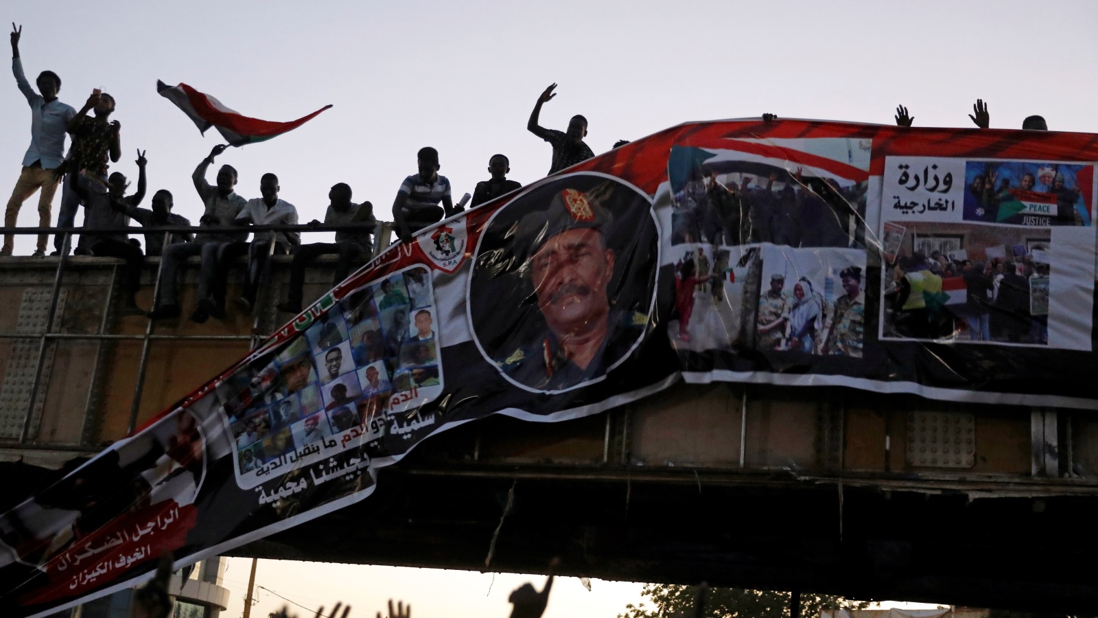 ‪متظاهرون ينزعون لافتة لرئيس المجلس العسكري الانتقالي من على جسر في العاصمة السودانية‬ (رويترز)