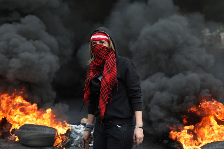 A demonstrator stands near a burning fire blocking a road, during a protest against the fall in Lebanese pound currency and mounting economic hardships, in Zouk, Lebanon March 8, 2021. REUTERS/Mohamed Azakir
