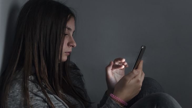 She is a victim of online social networks. Sad teen checking phone sitting on the floor in the living room at home with a dark background. Victim of online bullying Stalker social networks