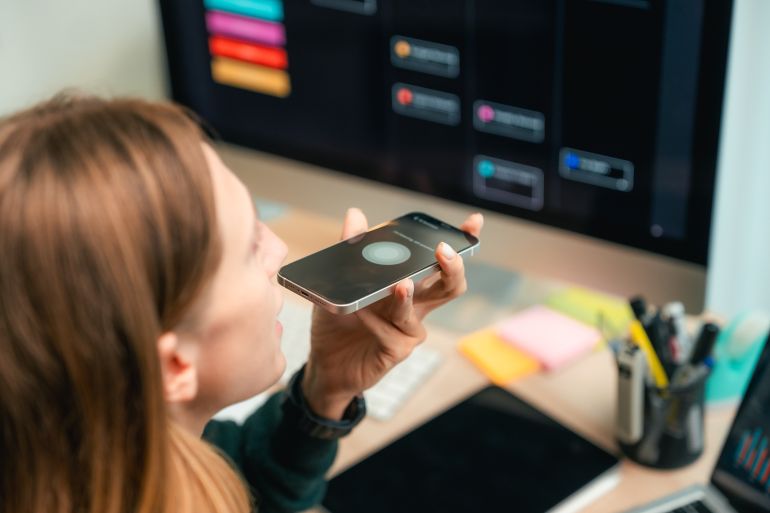 Modern woman using voice commands on her smartphone to interact with AI assistant app, efficiently managing her work schedule hands-free to stay productive and organized during a busy remote workday adobe stock